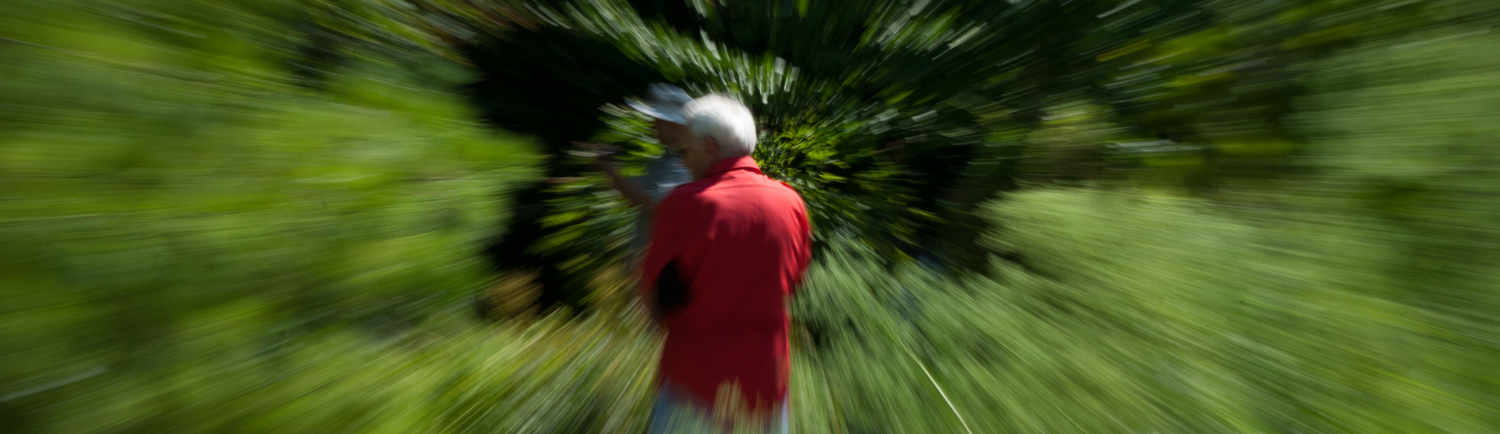 Person in red shirt experiencing dizziness with blurred motion effect in green outdoor setting