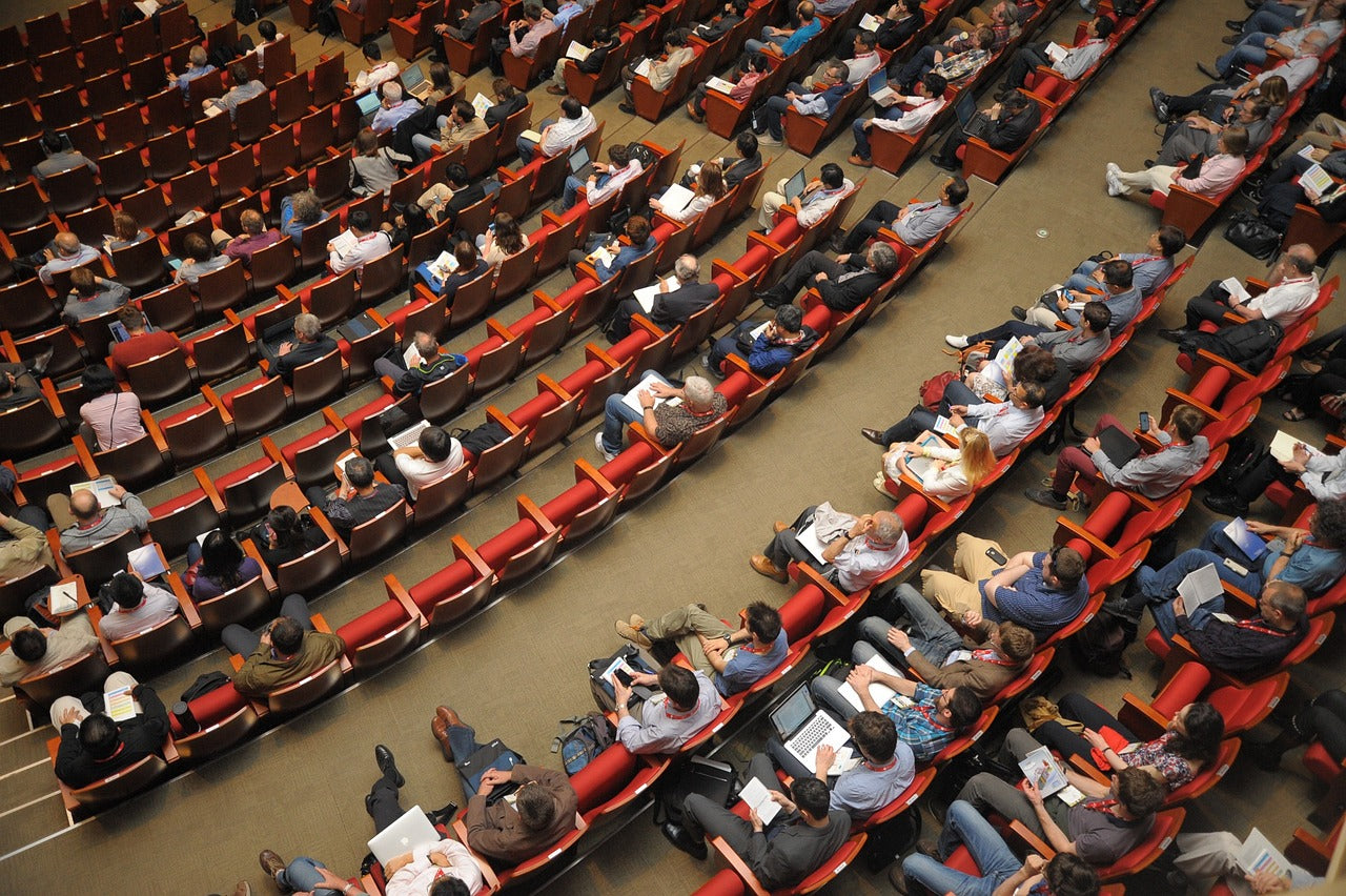 Large audience attending a professional conference in a modern auditorium with red seats.