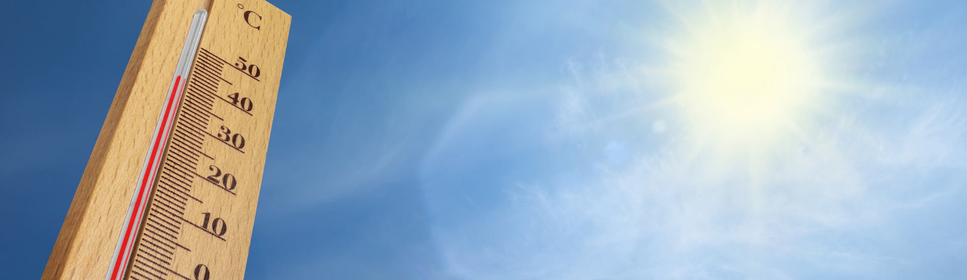 Thermometer showing high temperatures against a clear blue sky with bright sunlight, indicating hot weather.