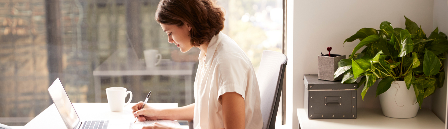 Woman sitting at desk with laptop and coffee, illustrating modern work-from-home setup and risks of sitting and poor circulation.